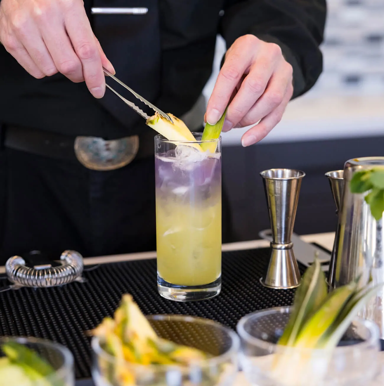 Bartender garnishing a layered cocktail with pineapple at a professional bar