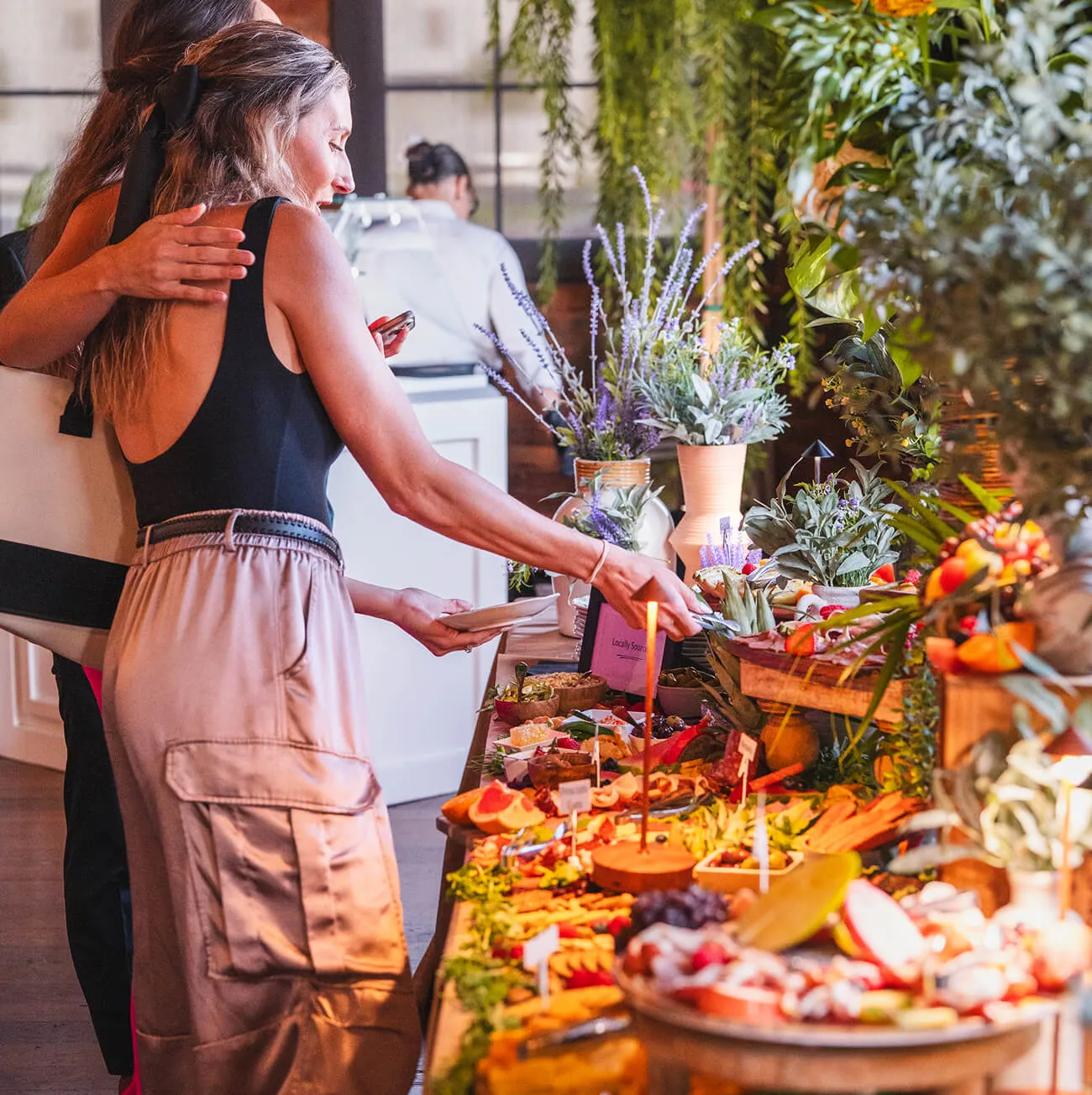 Guest selecting food from a lavish grazing table with charcuterie and fresh fruit