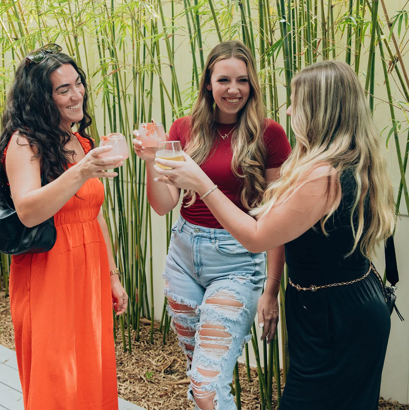 Guests toasting with colorful cocktails in front of a bamboo wall