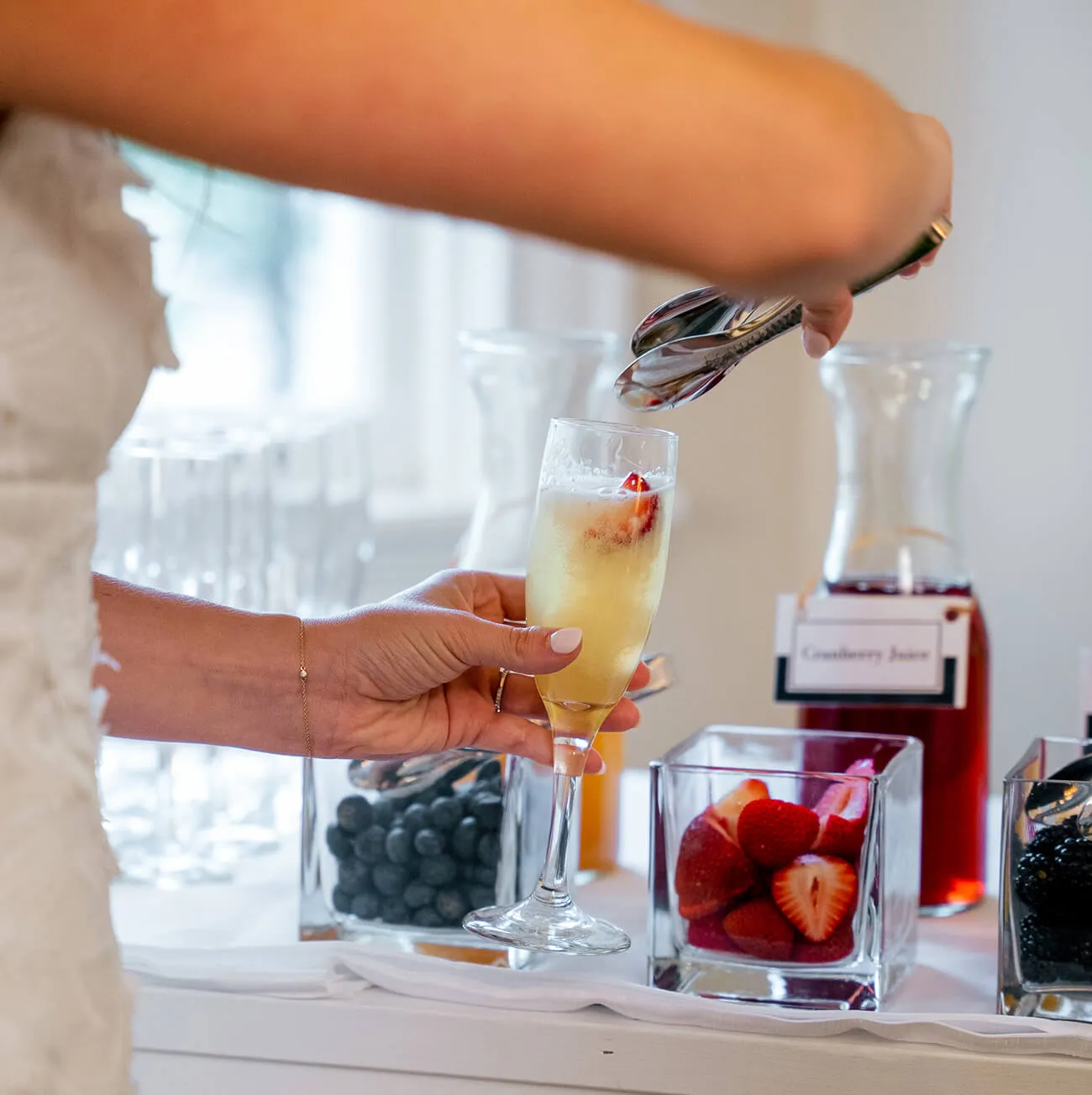Bride garnishing a mimosa with fresh berries at a wedding beverage station