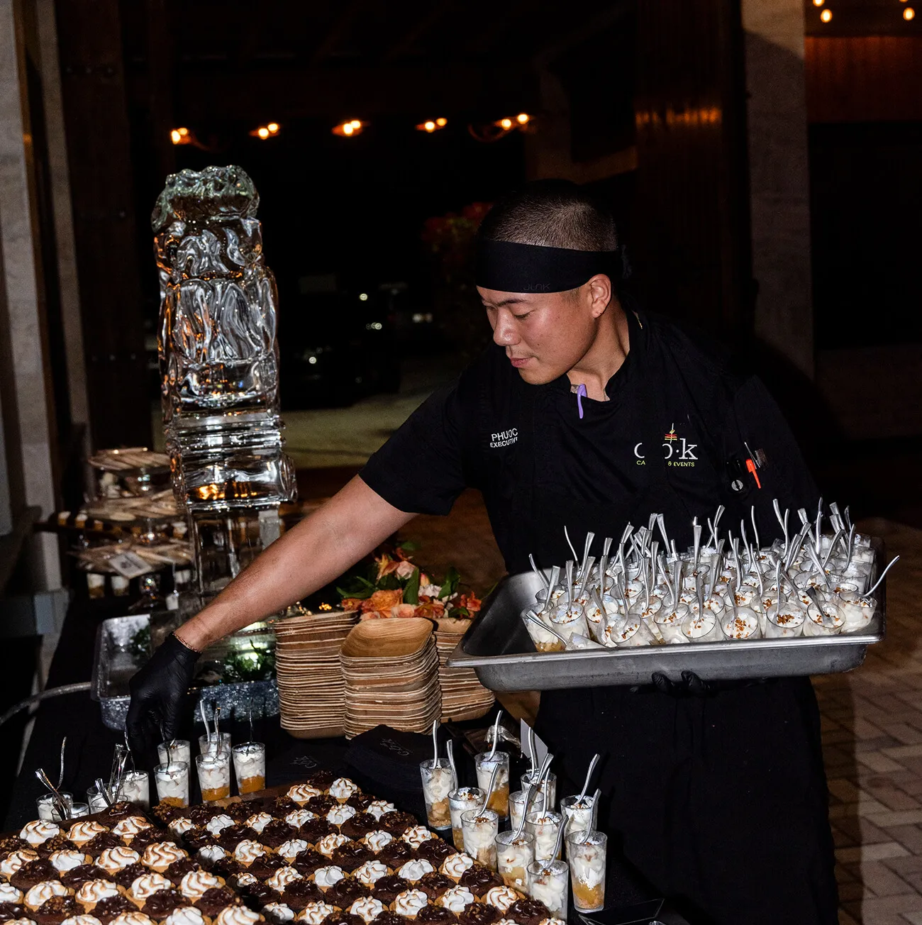 Executive chef arranging miniature desserts beside an ice sculpture at an evening event