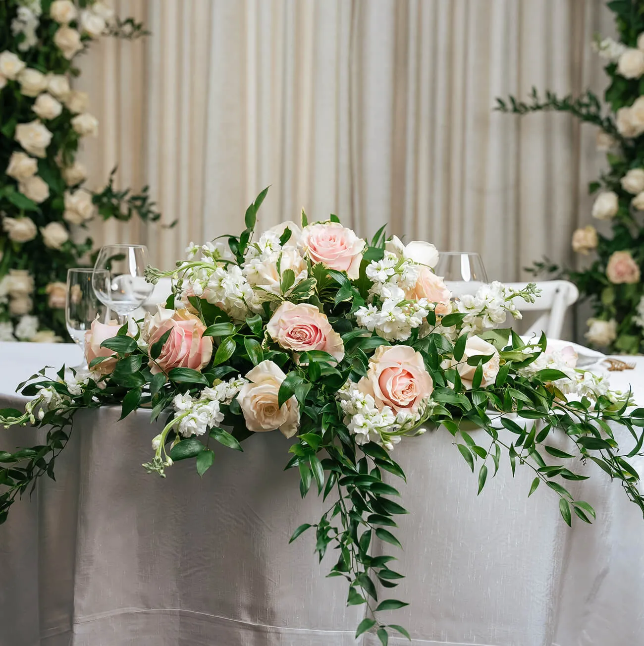 Lush floral centerpiece with blush roses and trailing greenery on a wedding table