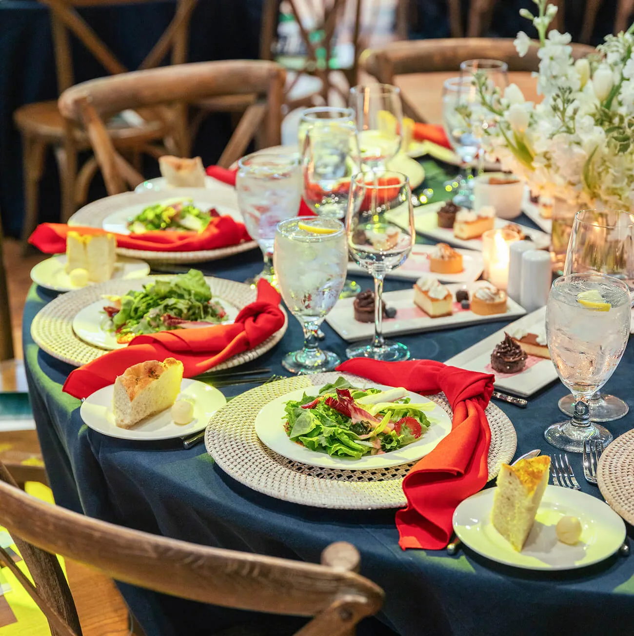 Formal dinner table with plated salads, dessert platters, and floral centerpiece