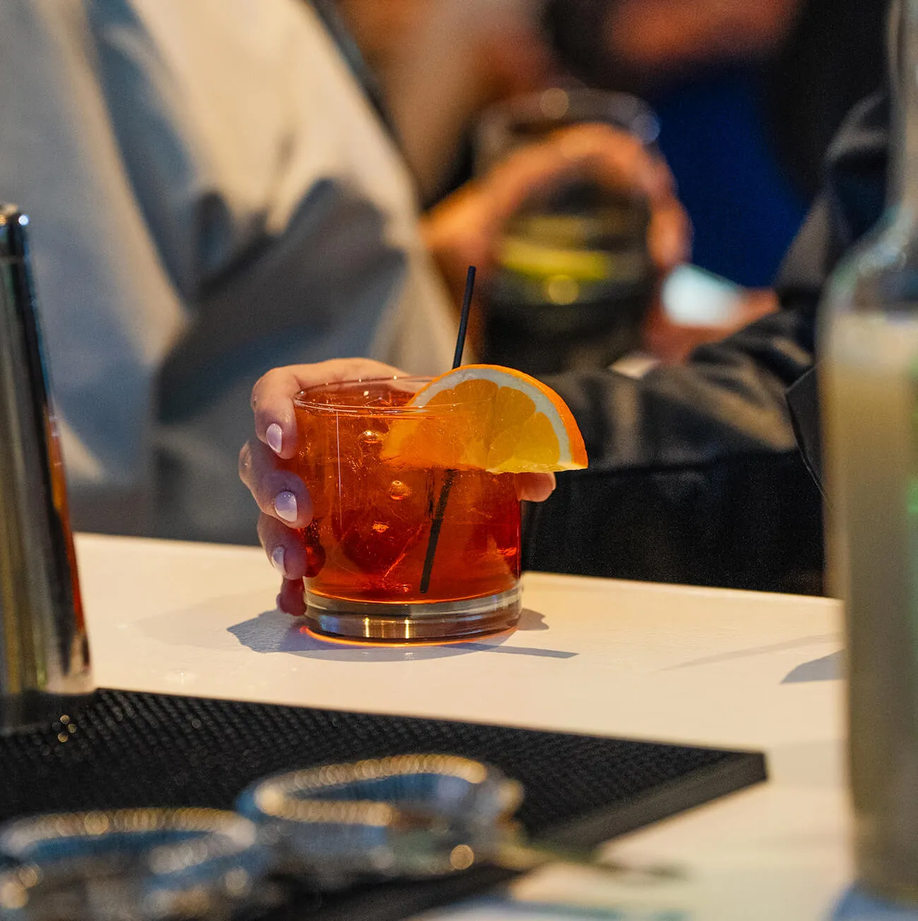 Hand holding a vibrant orange cocktail garnished with a citrus slice at the bar