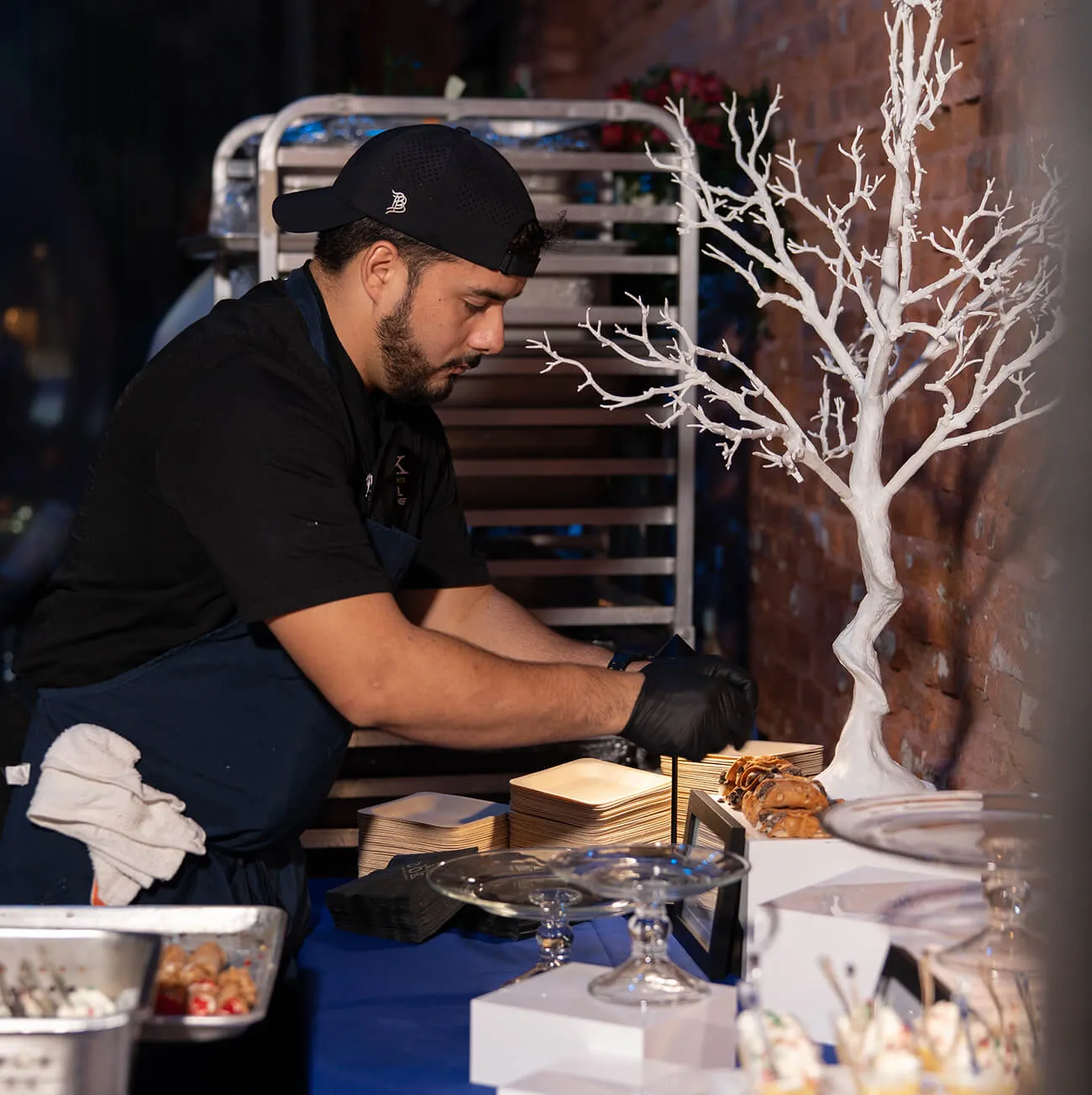 Chef arranging pastries on a dessert station with decorative tree centerpiece
