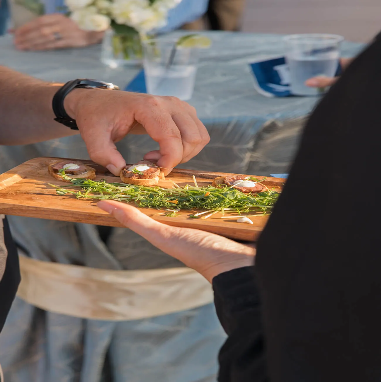 Guest reaching for a seared meat crostini from a passed wooden serving board