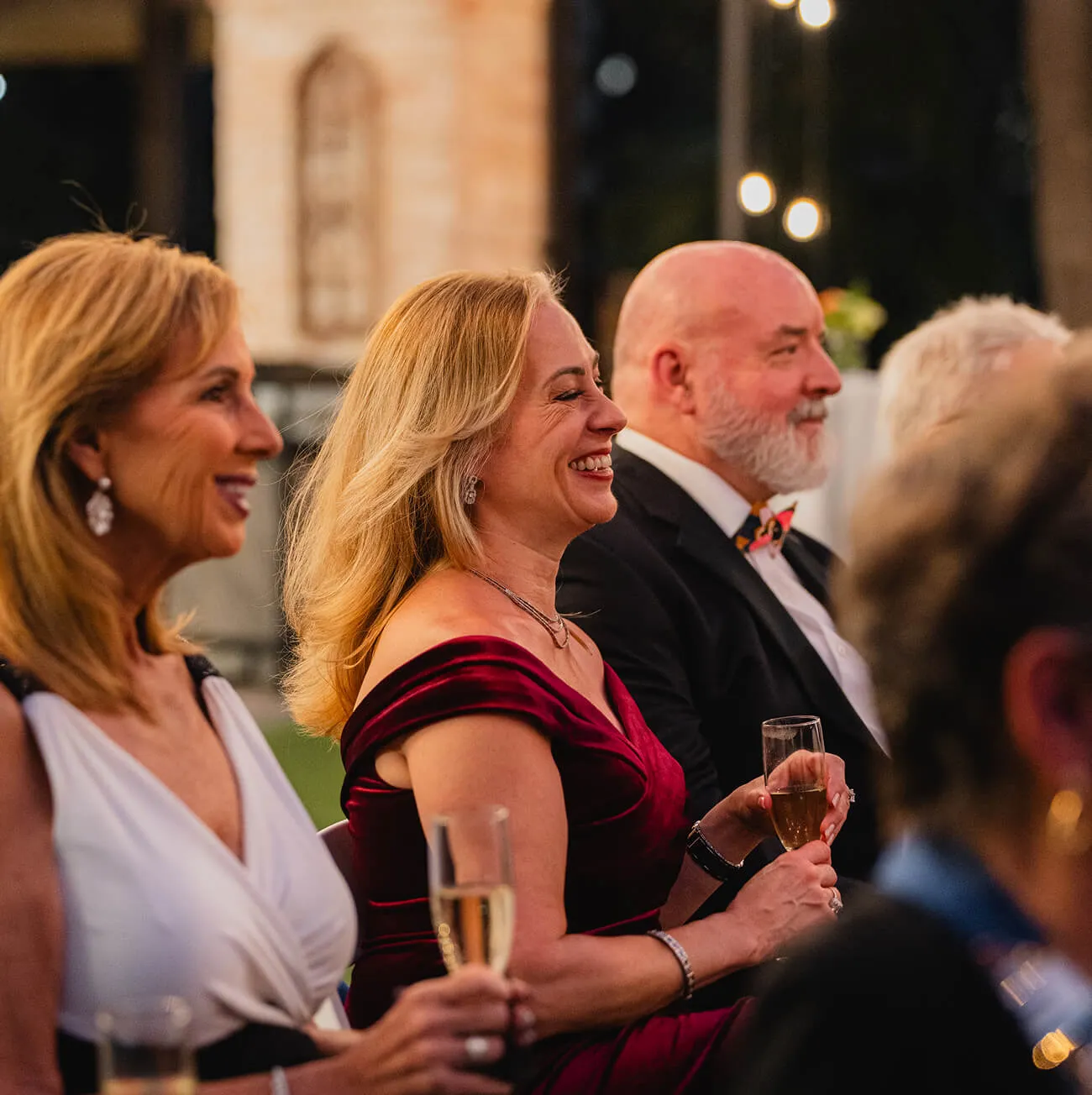 Guests laughing and enjoying champagne at a formal outdoor evening reception