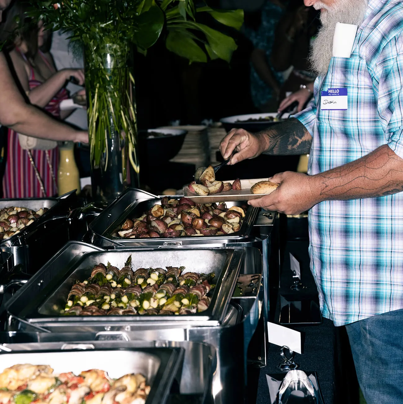 Guest serving roasted potatoes and asparagus from a chafing dish buffet line