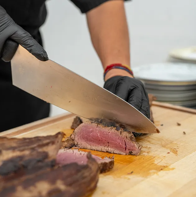 Chef slicing medium-rare roast beef on a wooden cutting board