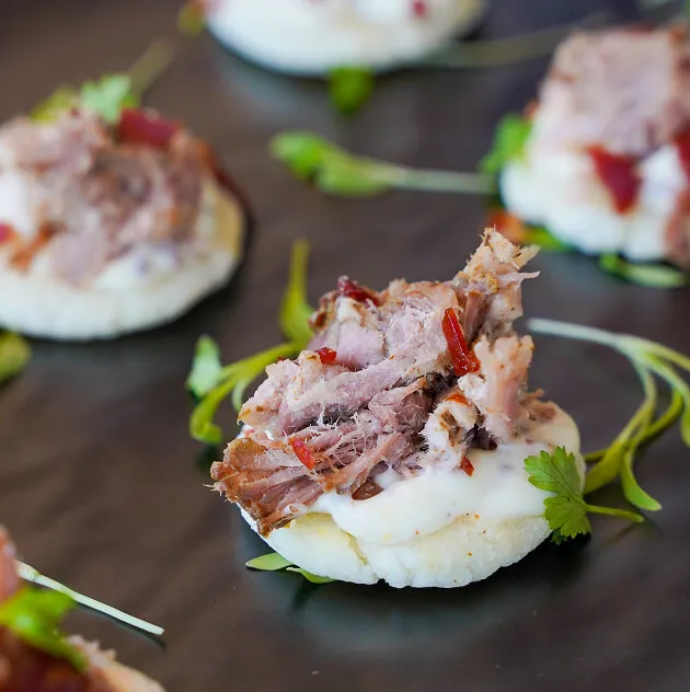 Canapes topped with pulled protein and microgreens