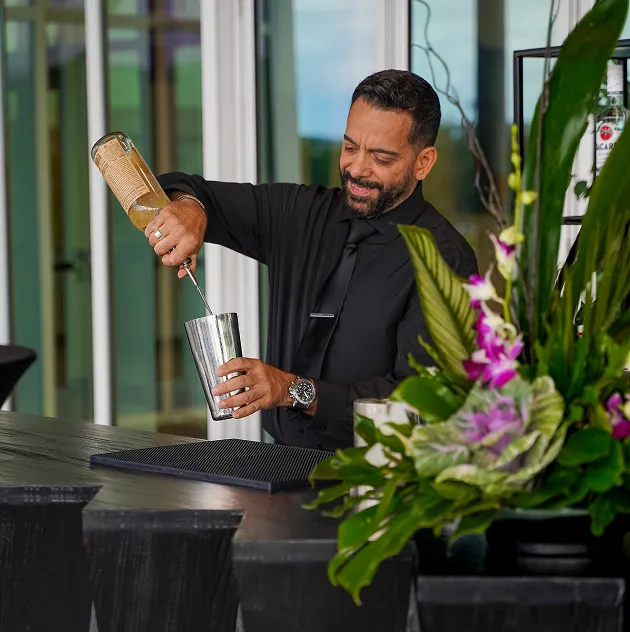 Bartender preparing a cocktail with a floral bar arrangement